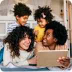 A couple look at a tablet with their two young children.  